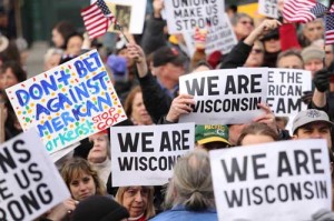 a crowd of people at the demonstration, who hold signs that says "we are wisconsin"